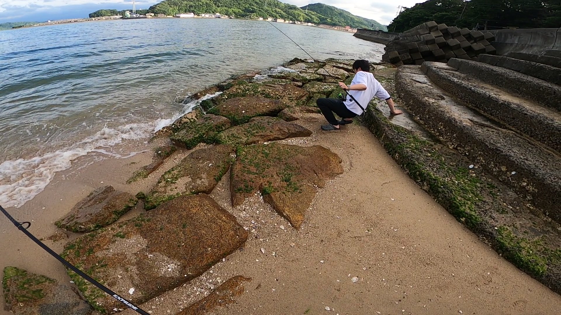 波打ち際の苔むした石場で釣り（後ろ姿）